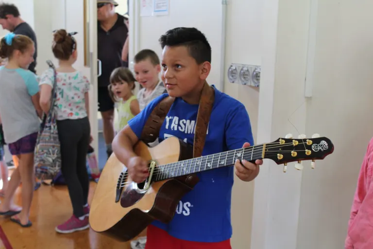Boy playing guitar as kids gather around